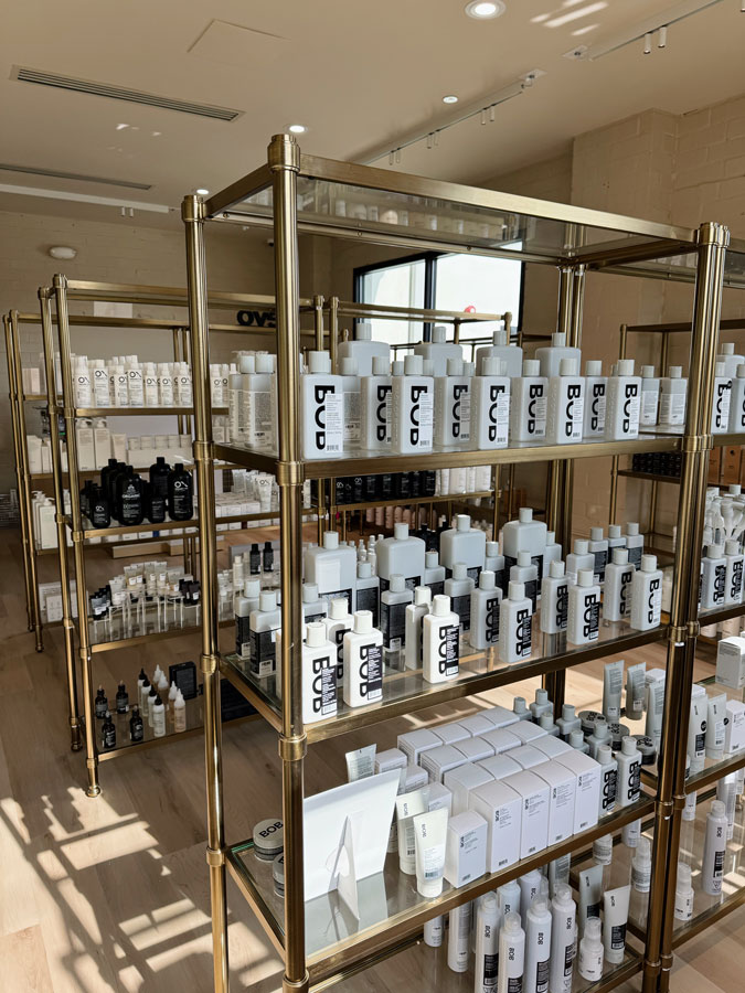 Shelves with neatly arranged bottles and boxes of hair and skincare products in a well-lit store with wooden flooring. - HC Beauty in Charlotte, Nc