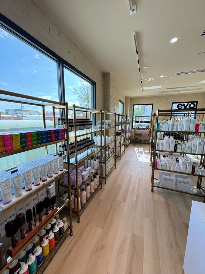 Shelves in a well-lit beauty supply store display various hair and skincare products, including bottles, brushes, and boxed items, next to large windows. - HC Beauty in Charlotte, Nc