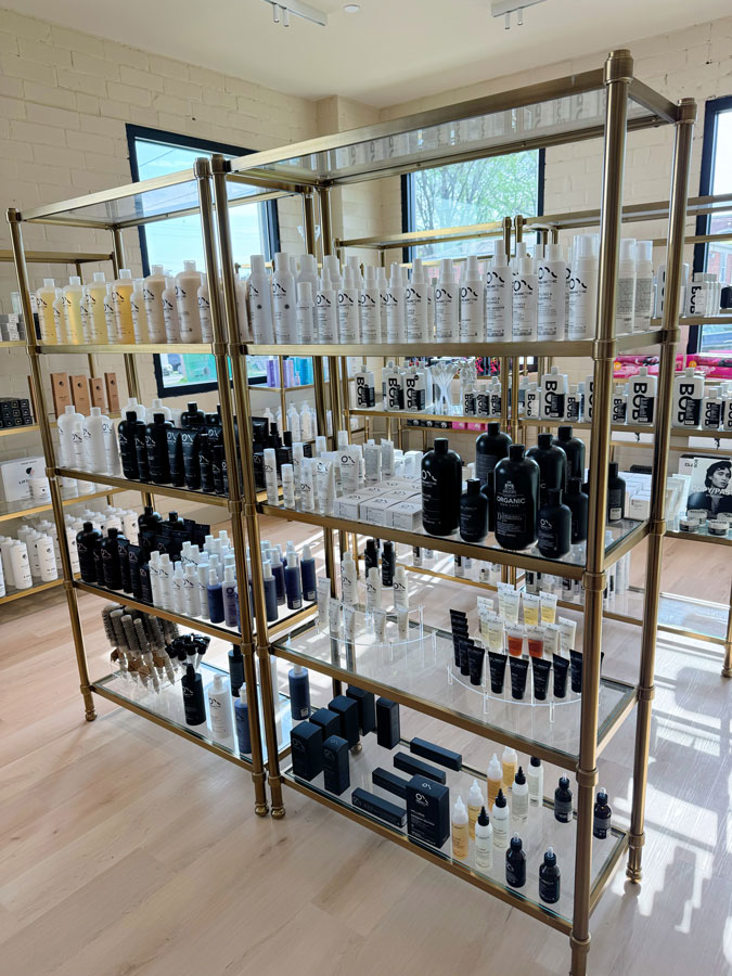 Metal shelves display neatly organized hair and beauty products in bottles and boxes in a well-lit store with large windows. - HC Beauty in Charlotte, Nc