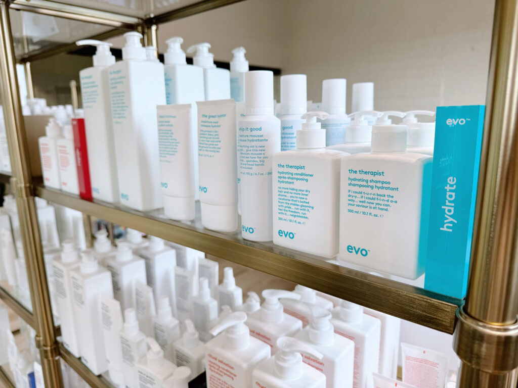 Shelves stocked with various bottles and containers of Evo hair care products, including shampoos and conditioners, neatly arranged in rows. - HC Beauty in Charlotte, Nc