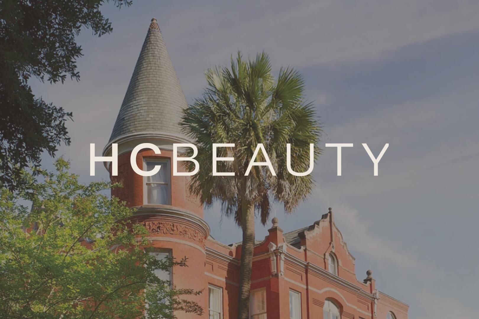 A red brick building with a pointed turret and palm tree in front, under a blue sky. The word “HCBEAUTY” is overlaid in white text. - HC Beauty in Charlotte, Nc