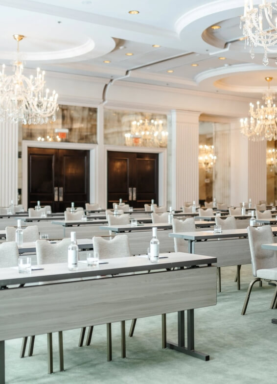 A conference room with rows of tables and chairs, each set with bottled water, notepads, and pens. Chandeliers and mirrored walls are visible in the background. - HC Beauty in Charlotte, Nc